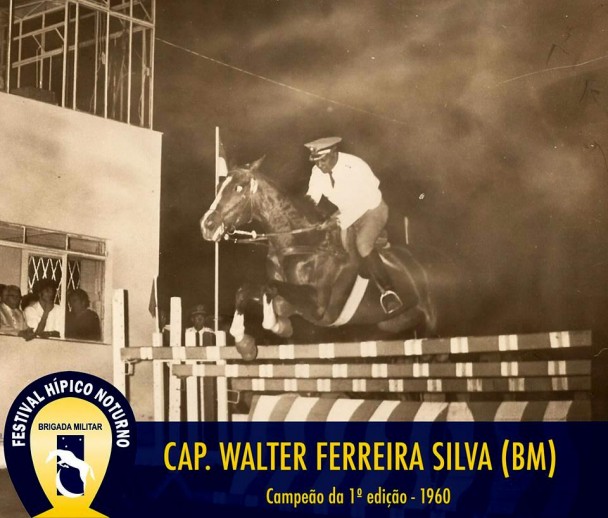  Cap Walter Ferreira da Silva saltando sobre barreira, montado em um cavalo preto com manchas brancas, durante a noite.