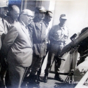 Ildo Meneghetti junto a grupo de oficiais uniformizados, olhando para a frente , em frente a uma arma, na sede do 2º Batalhão Policial.