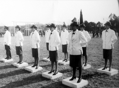 Grupo de oficiais do sexo feminino, usando blazer branco e saia até o joelho, de chapéu, agrupadas em duas fileiras.